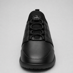 A black low-top sneaker shown from a front-facing perspective against a light gray background. The shoe features a matte black leather upper with a textured synthetic panel on the side, matching black laces, and a small winged emblem on the tongue.