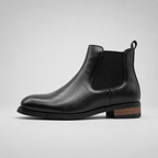 A black leather Chelsea boot with a black elastic side panel and a low stacked heel featuring a brown wood inlay, shown in profile against a light gray background.